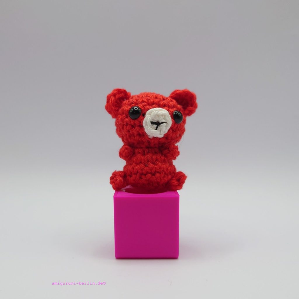 ein signalroter gehäkelter Bär auf einem pinkfarbenen Block a signal red crocheted bear on a pink block