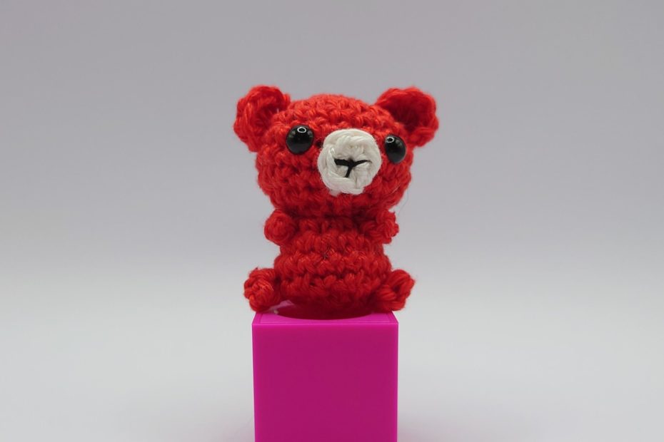 ein signalroter gehäkelter Bär auf einem pinkfarbenen Block a signal red crocheted bear on a pink block