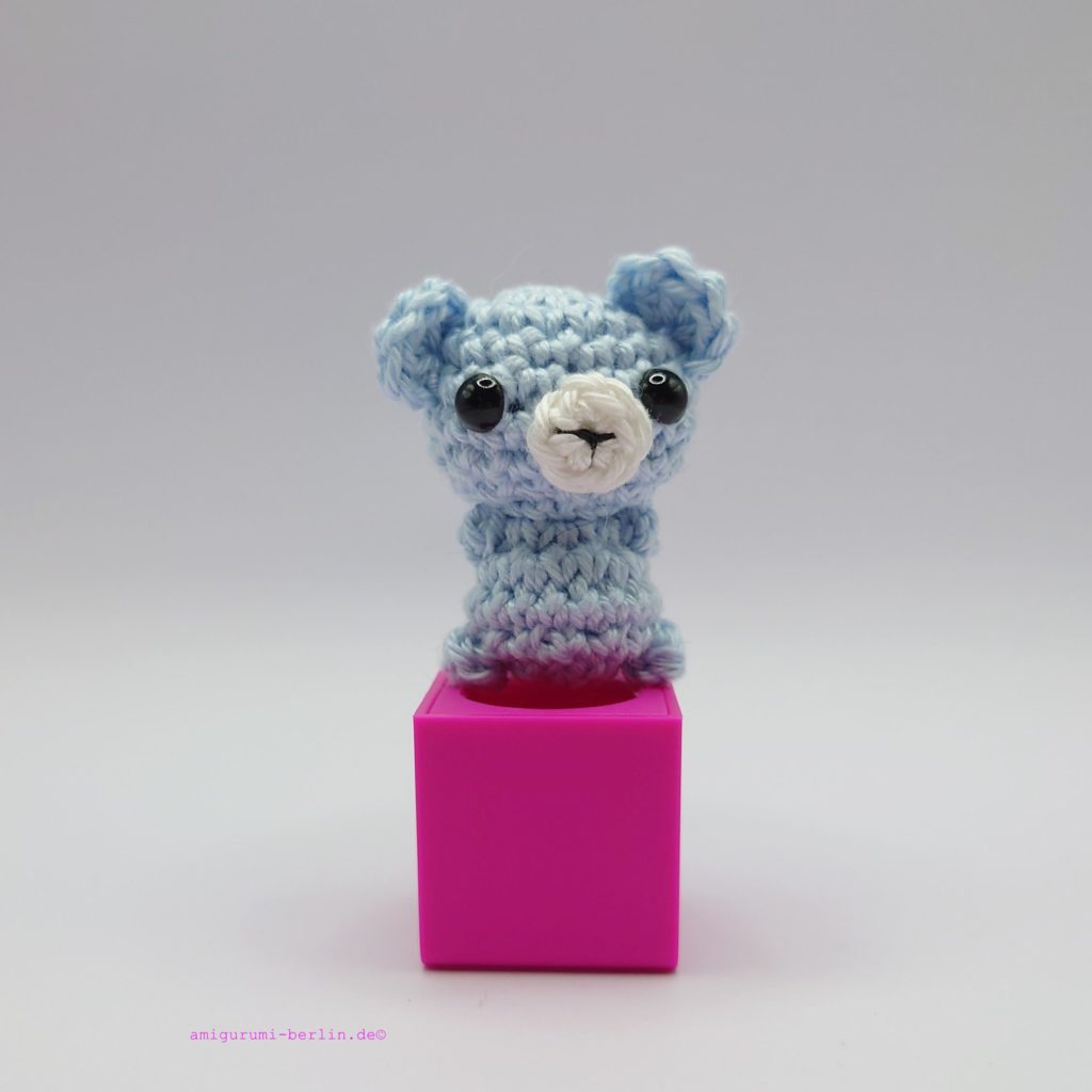 ein eisblauer gehäkelter Bär auf einem pinkfarbenen Block - an ice blue crocheted bear on a pink block