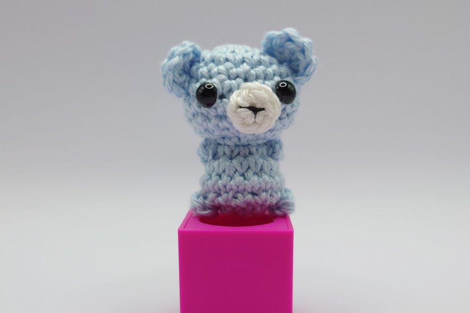 ein eisblauer gehäkelter Bär auf einem pinkfarbenen Block - an ice blue crocheted bear on a pink block