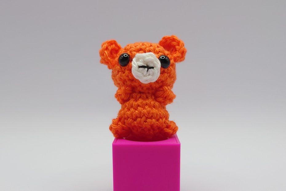 ein orangefarbener gehäkelter Bär auf einem pinkfarbenen Block - orange crocheted bear on a pink block