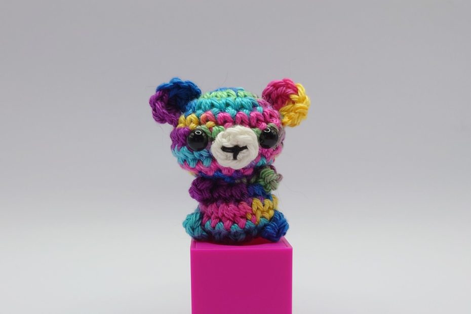 ein multifarbener gehäkelter Bär auf einem pinkfarbenen Block - a multi-colored crocheted bear on a pink block