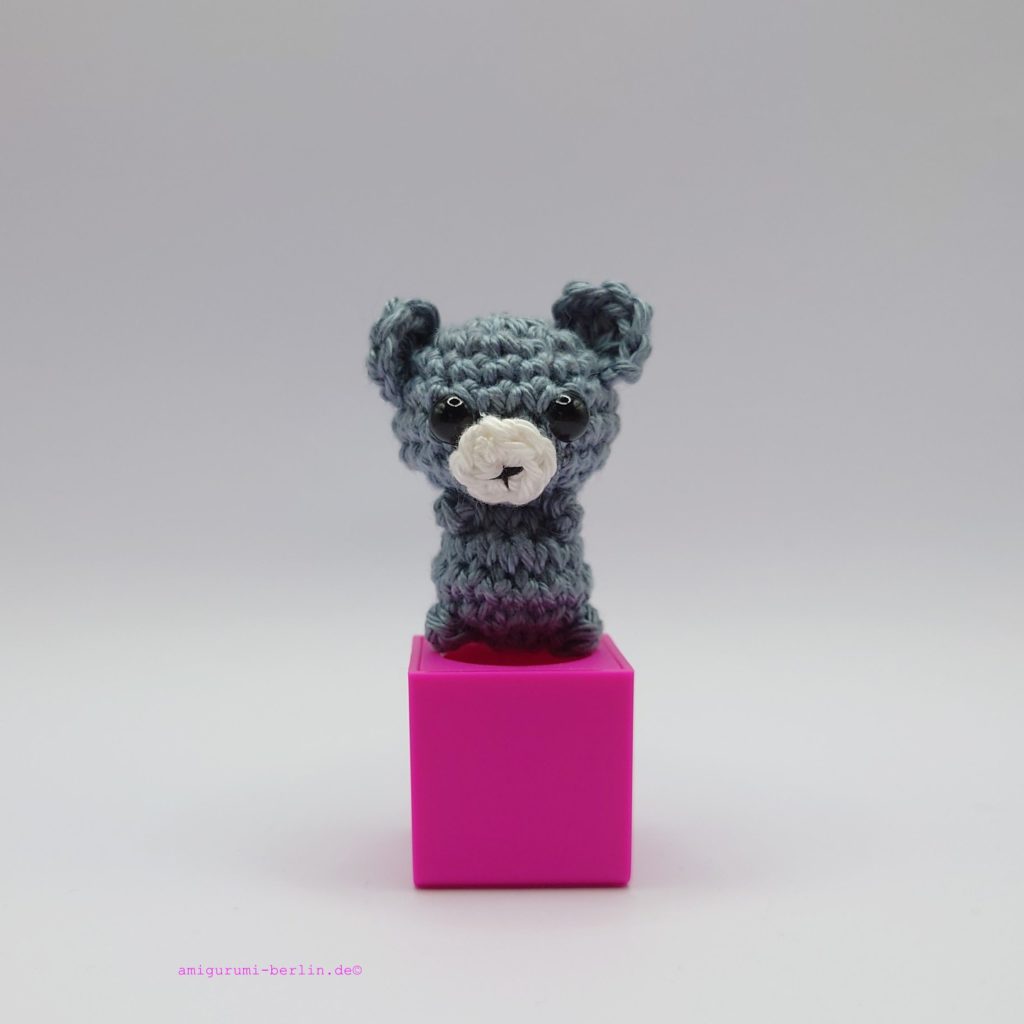 ein steinfarbener gehäkelter Bär auf einem pinkfarbenen Block - a stone-colored crocheted bear on a pink block