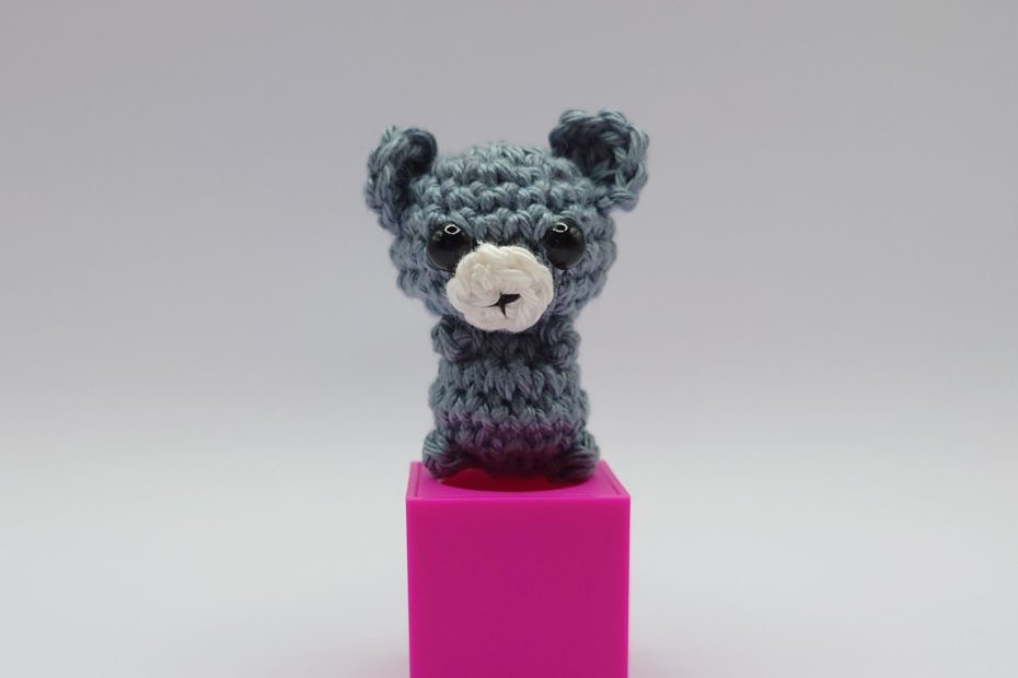 ein steinfarbener gehäkelter Bär auf einem pinkfarbenen Block - a stone-colored crocheted bear on a pink block