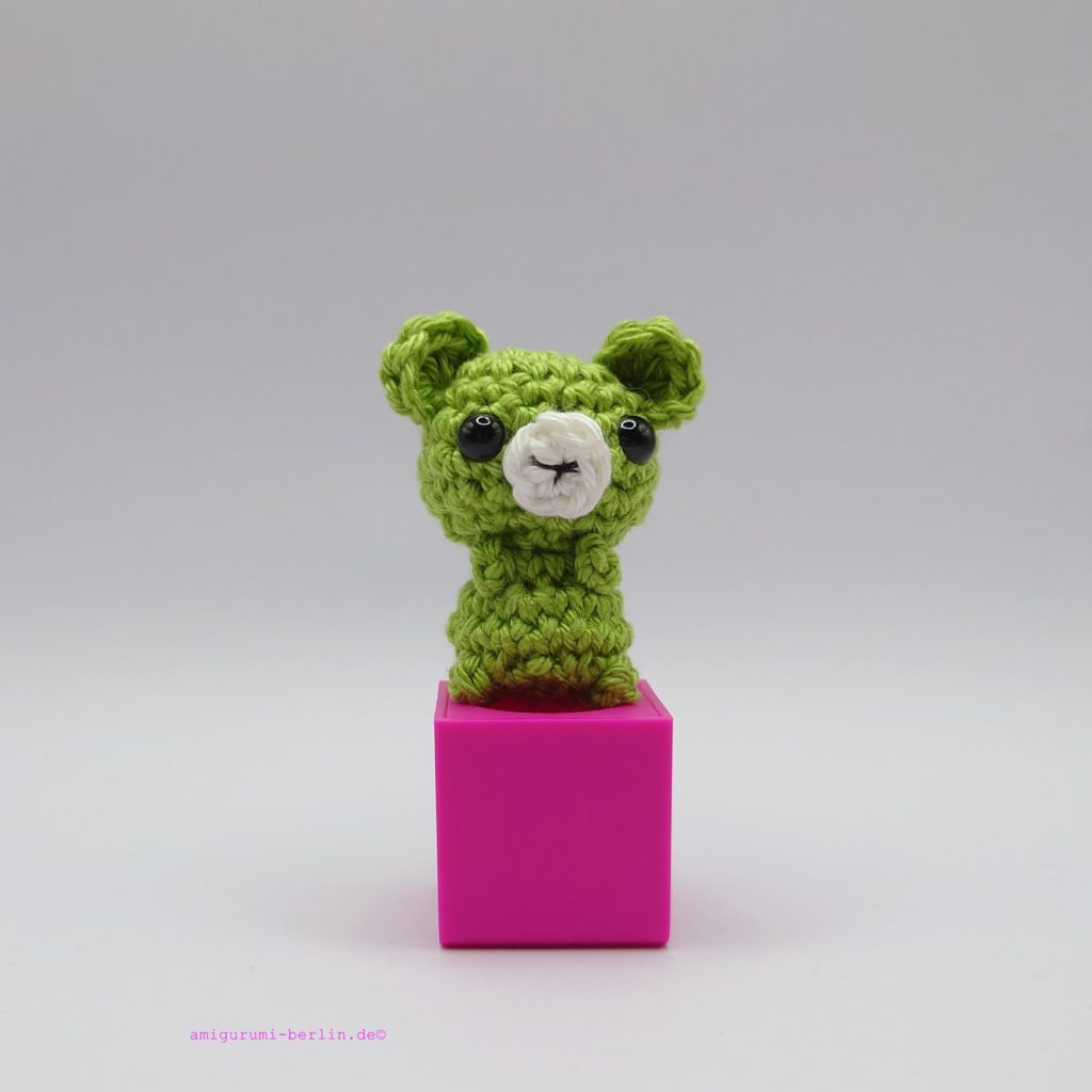 ein apfelfarbener gehäkelter Bär auf einem pinkfarbenen Block - an apple-colored crocheted bear on a pink block