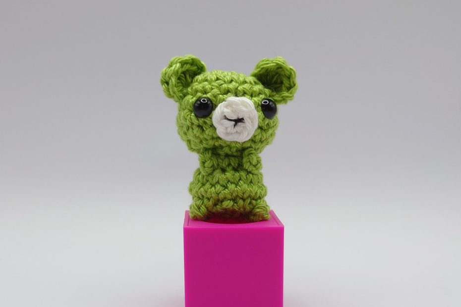 ein apfelfarbener gehäkelter Bär auf einem pinkfarbenen Block - an apple-colored crocheted bear on a pink block