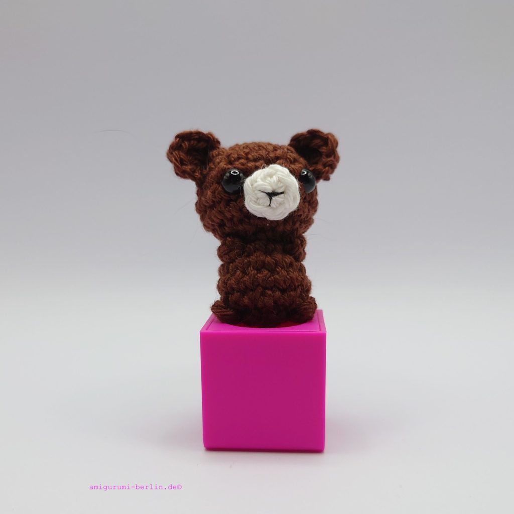 ein kaffeefarbener gehäkelter Bär auf einem pinkfarbenen Block - a coffee-colored crocheted bear on a pink block