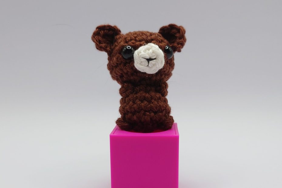 ein kaffeefarbener gehäkelter Bär auf einem pinkfarbenen Block - a coffee-colored crocheted bear on a pink block