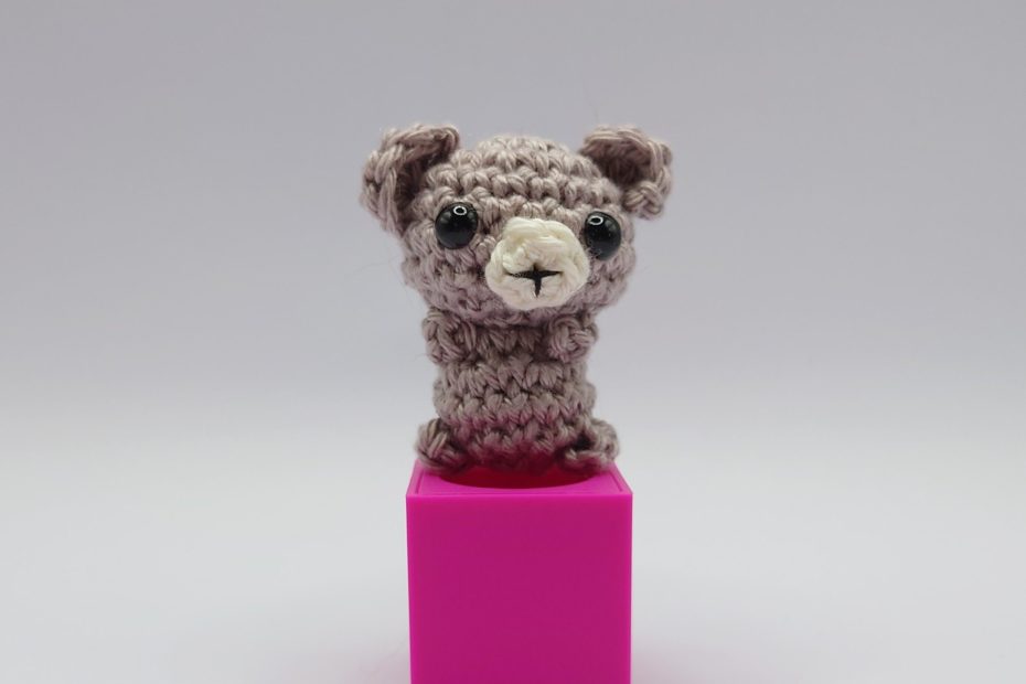 ein schlammfarbener gehäkelter Bär auf einem pinkfarbenen Block - a mud-coloured crocheted bear on a pink block