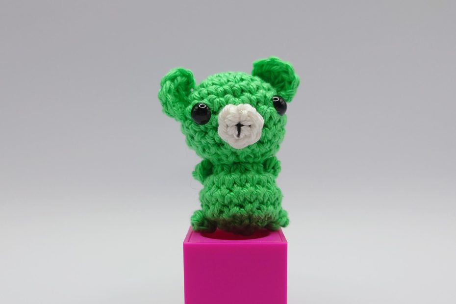 ein maigrüner gehäkelter Bär auf einem pinkfarbenen Block - a maygreen-coloured crocheted bear on a pink block